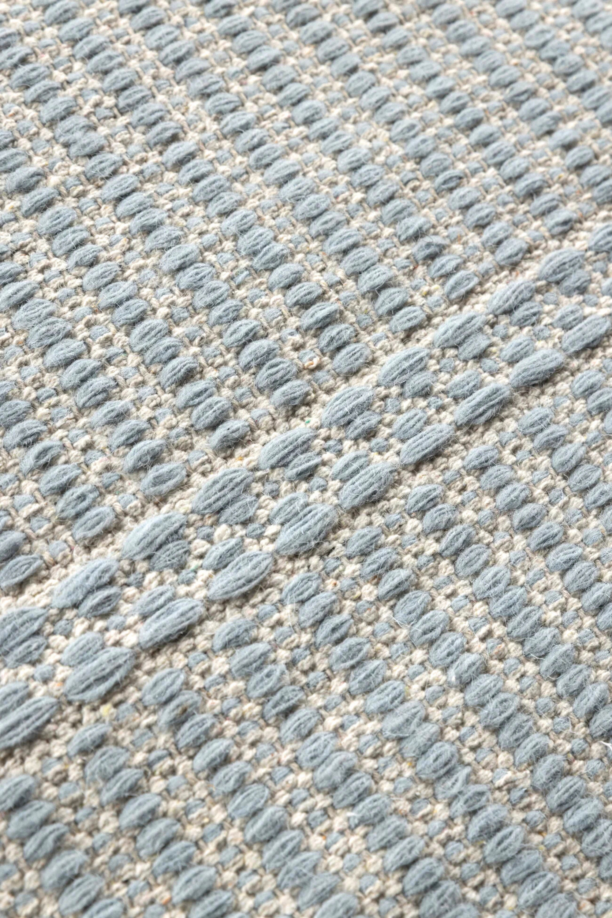 a closeup of a blue wool and cotton rug featuring a design inspired by ancient irish script