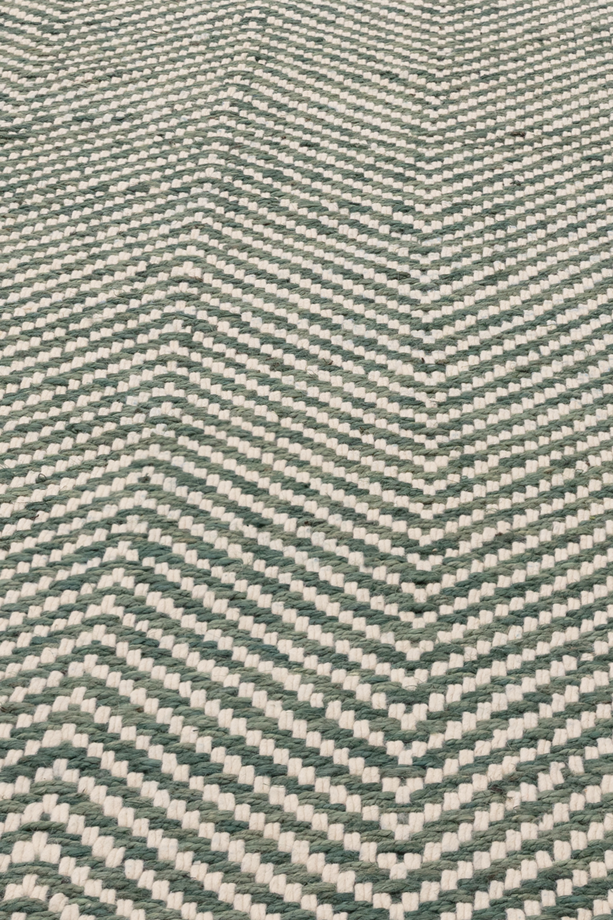 Textured woven rug with green and cream chevron pattern