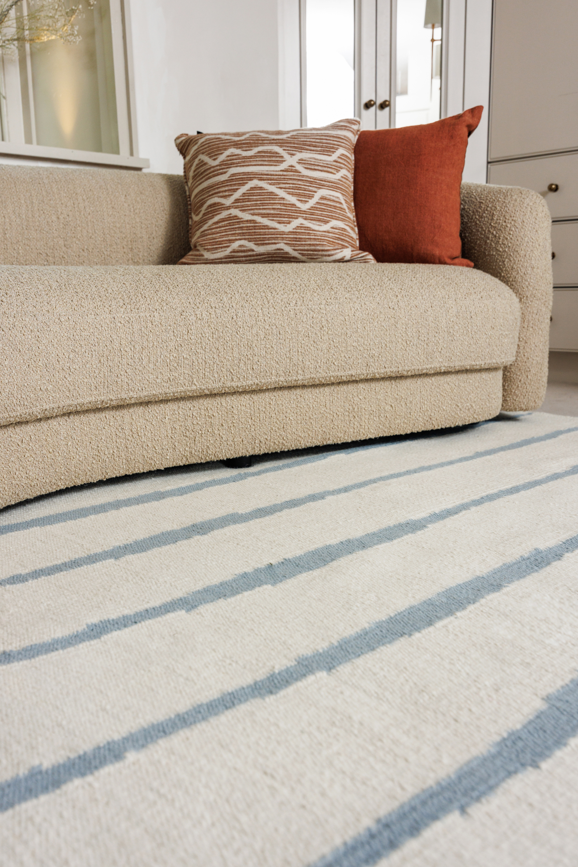Neutral ivory wool and cotton flatweave rug featuring blue ripple linear lines placed under a couch
