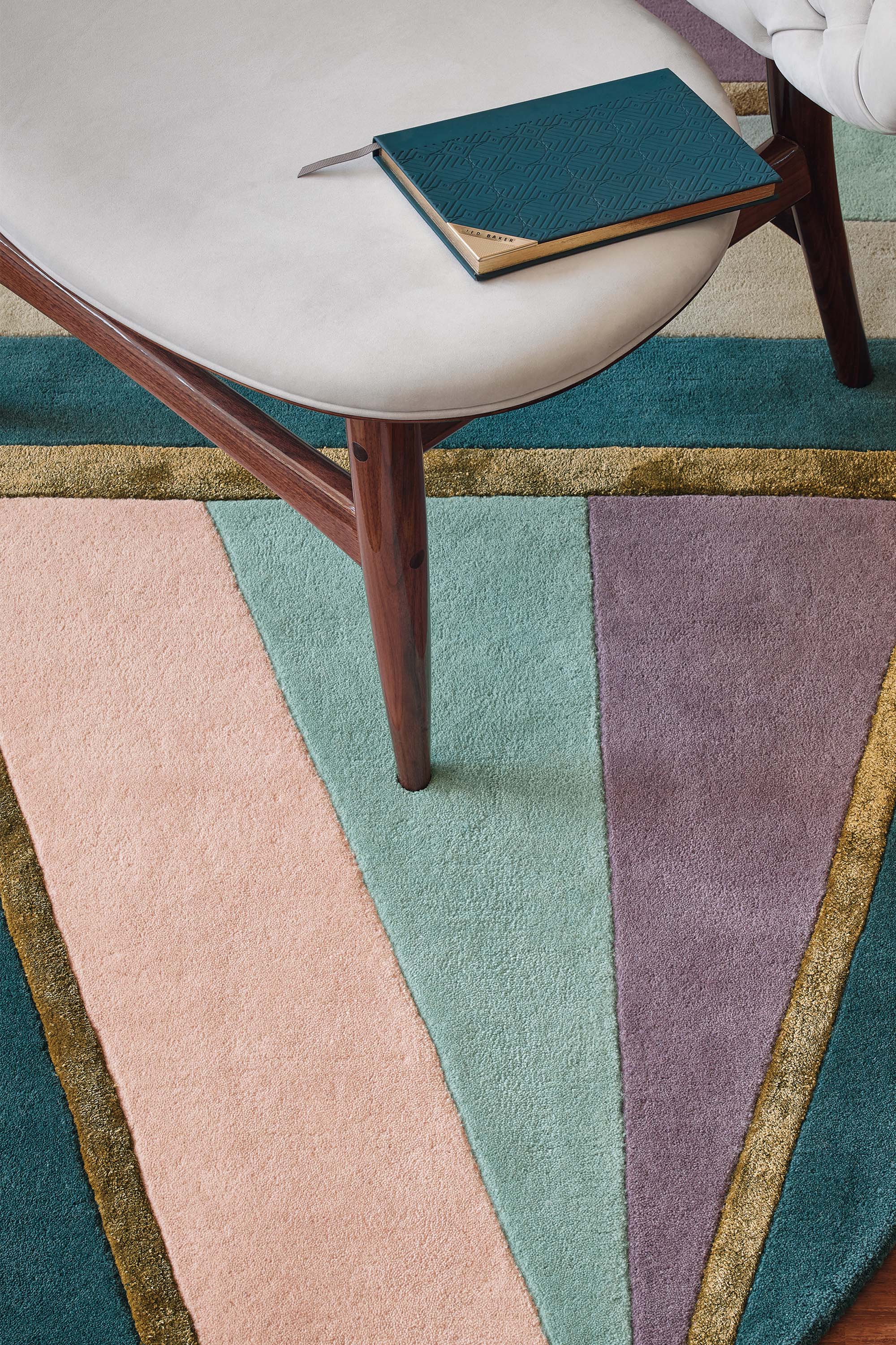 Rectangular rug with geometric stripe pattern in green, teal, grey and purple. Gold details.
