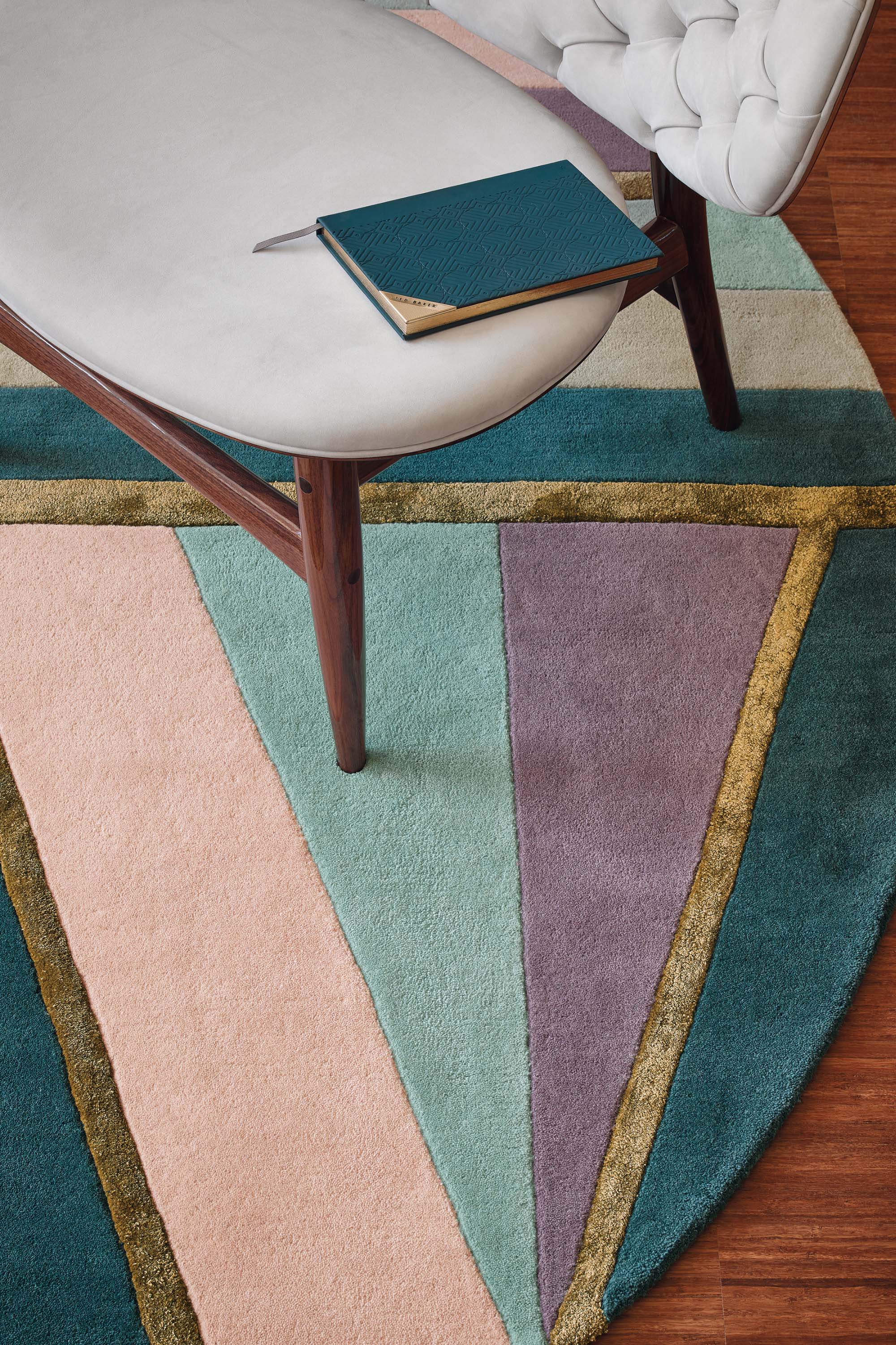 Round rug with geometric stripe pattern in green, teal, grey and purple. Gold details.
