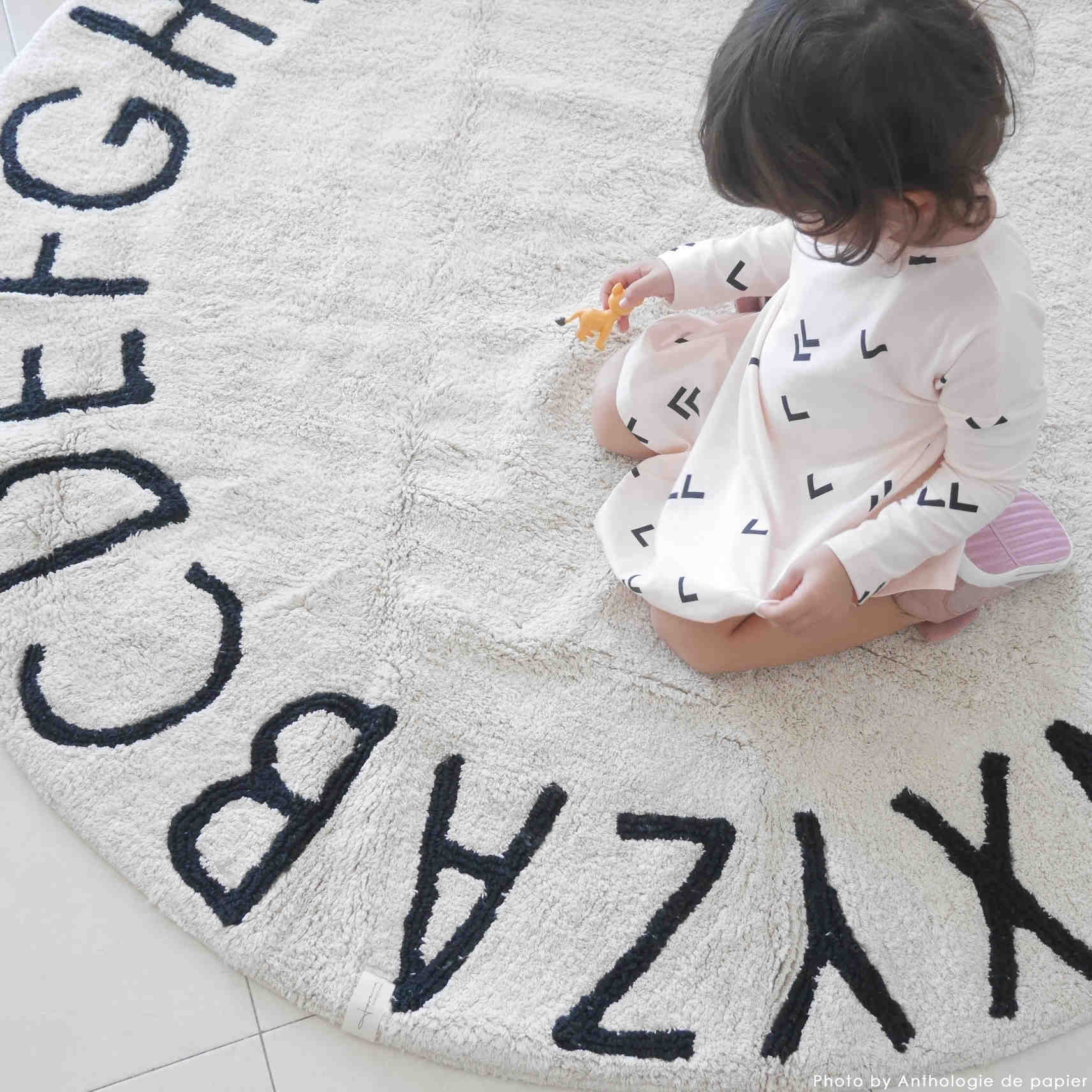Circular white cotton rug decorated with a black alphabet border