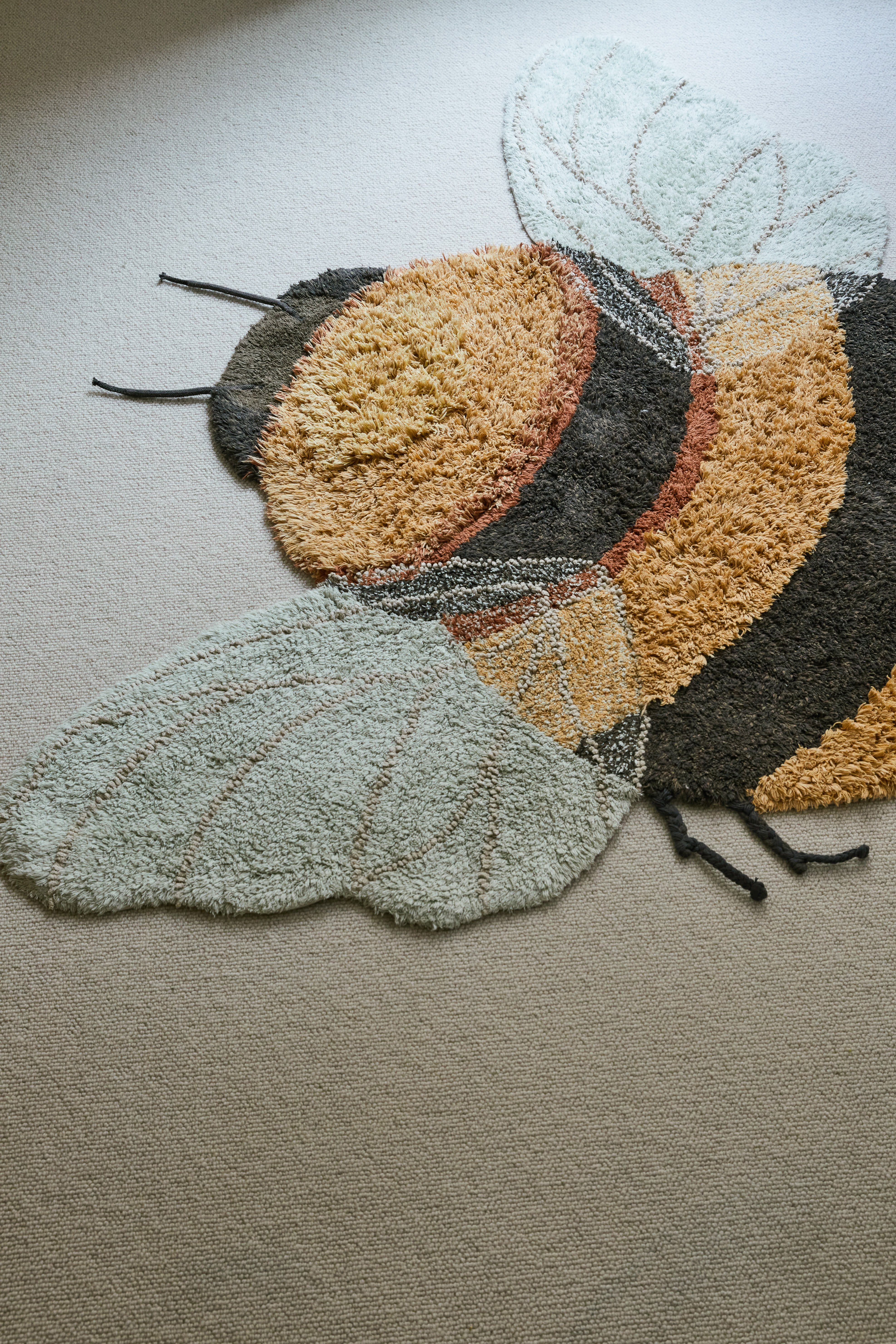 Bee-shaped rug with shades of gold, orange, brown, cream, and beige
