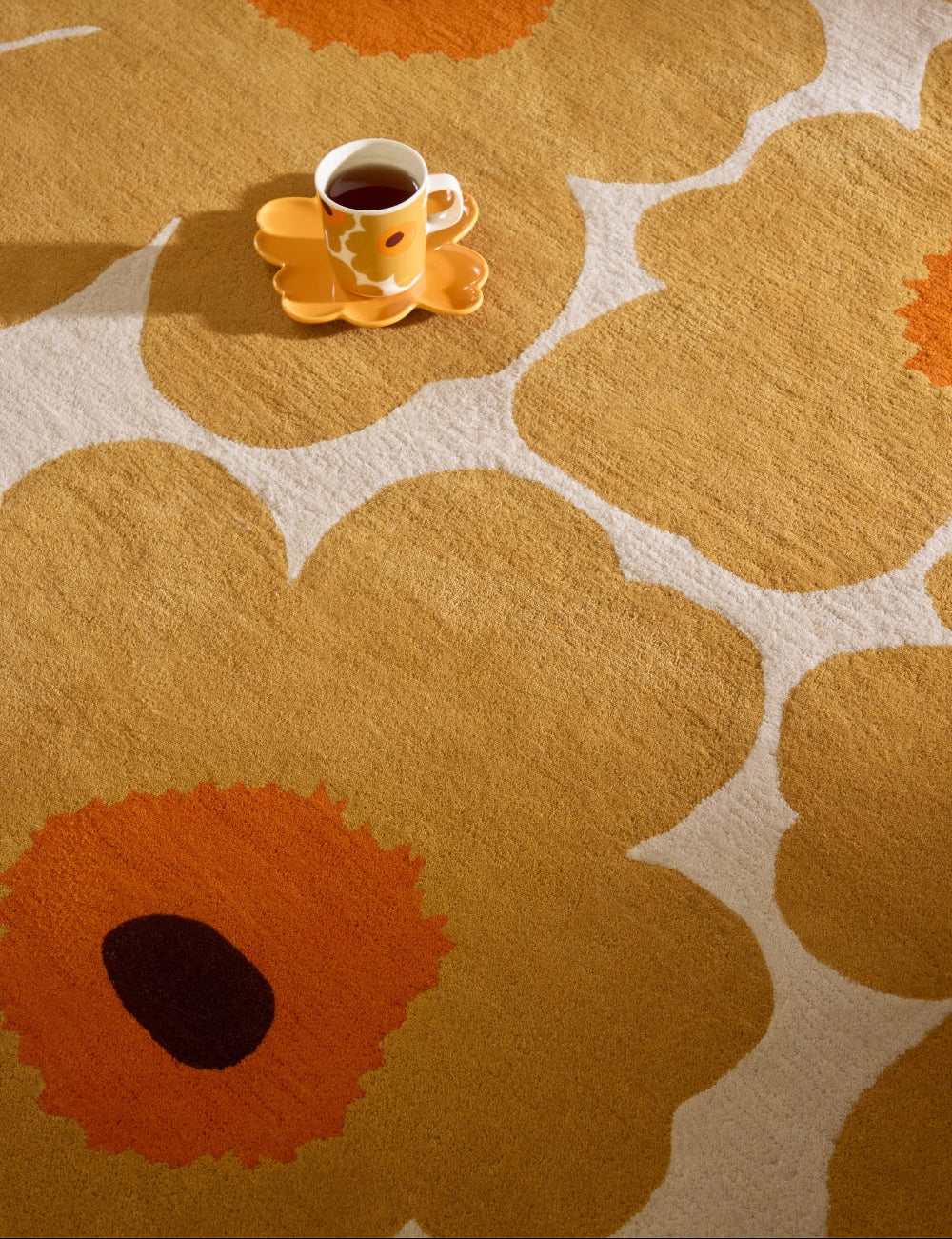 Cup of coffee on a floral-patterned wool rug with large orange flowers.