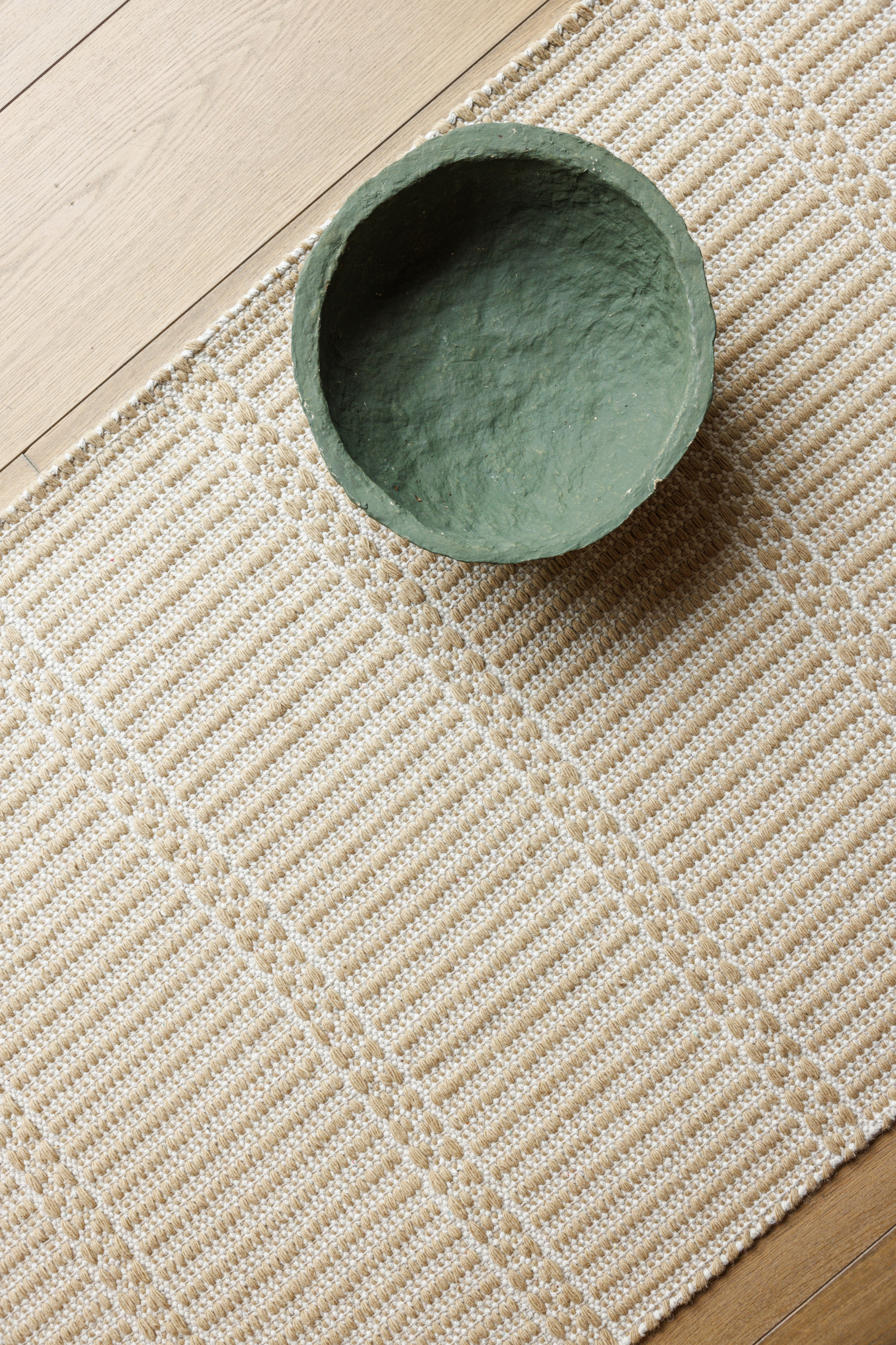a green bowl placed on a wool and cotton runner rug in a golden straw tone featuring a design inspired by ancient irish script
