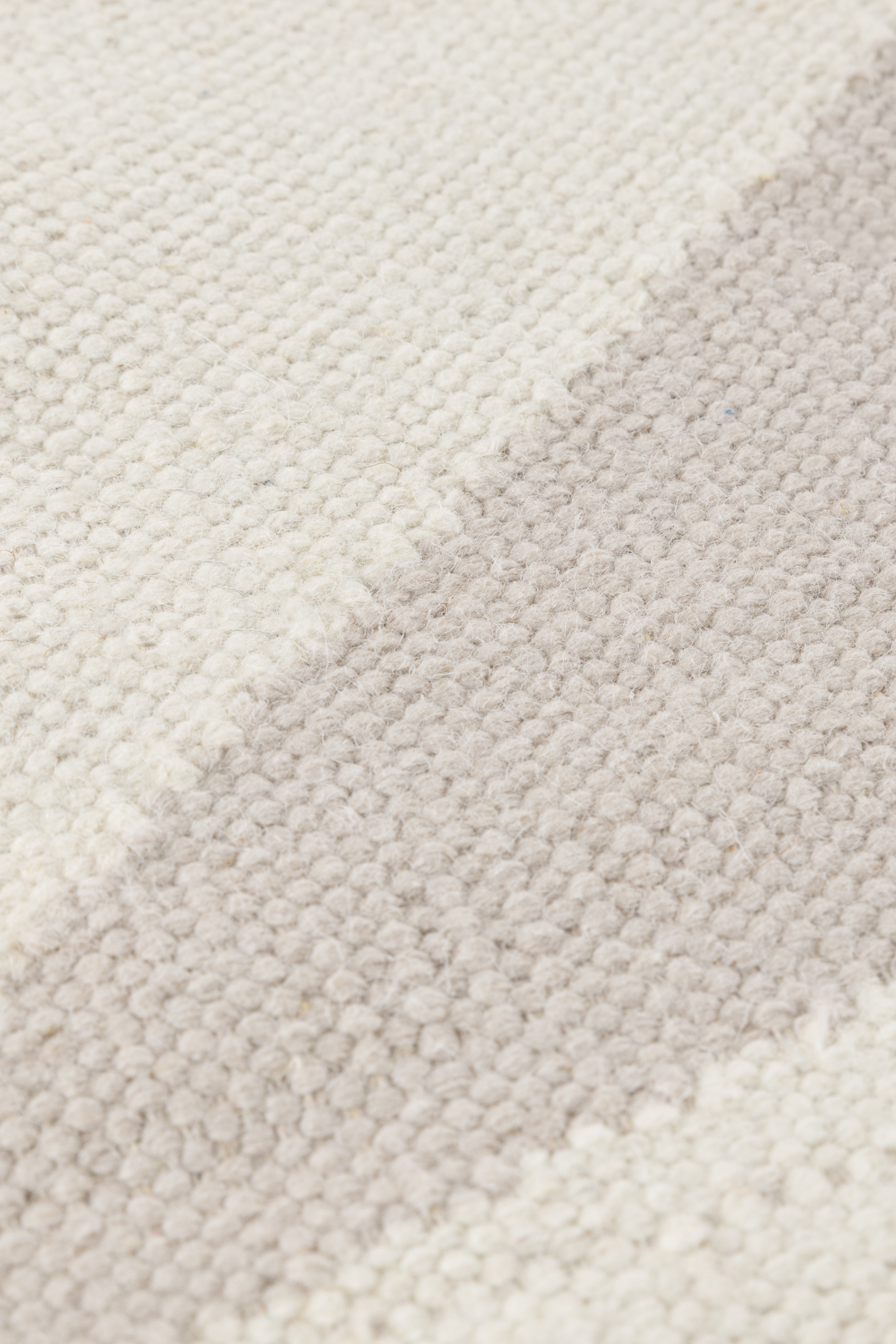 a close up of the pile of a neutral greige wool and cotton rug featuring an ivory angular design