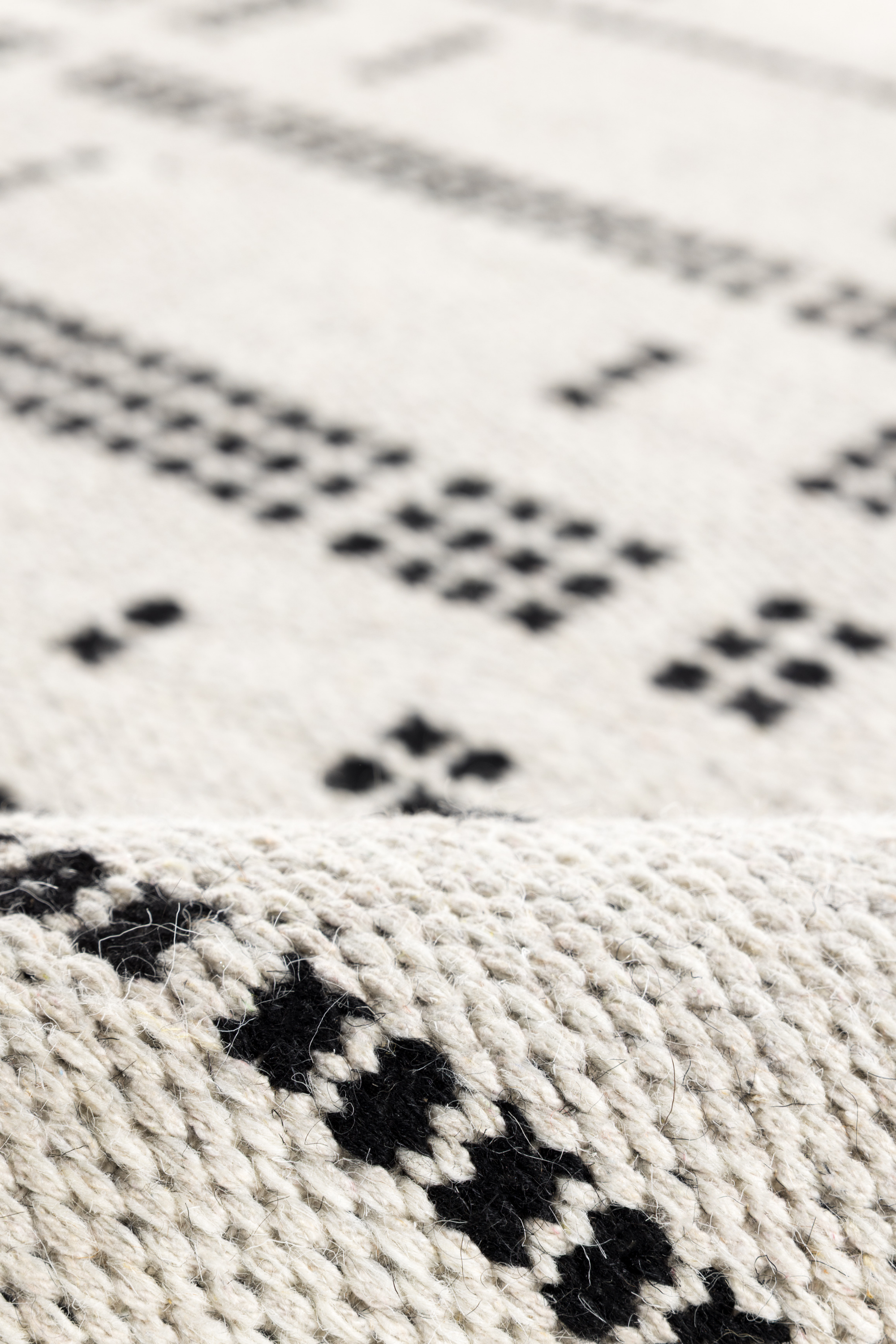 close up of a white wool and cotton rug with a black geometric pattern inspired by the Manhattan skyline at night