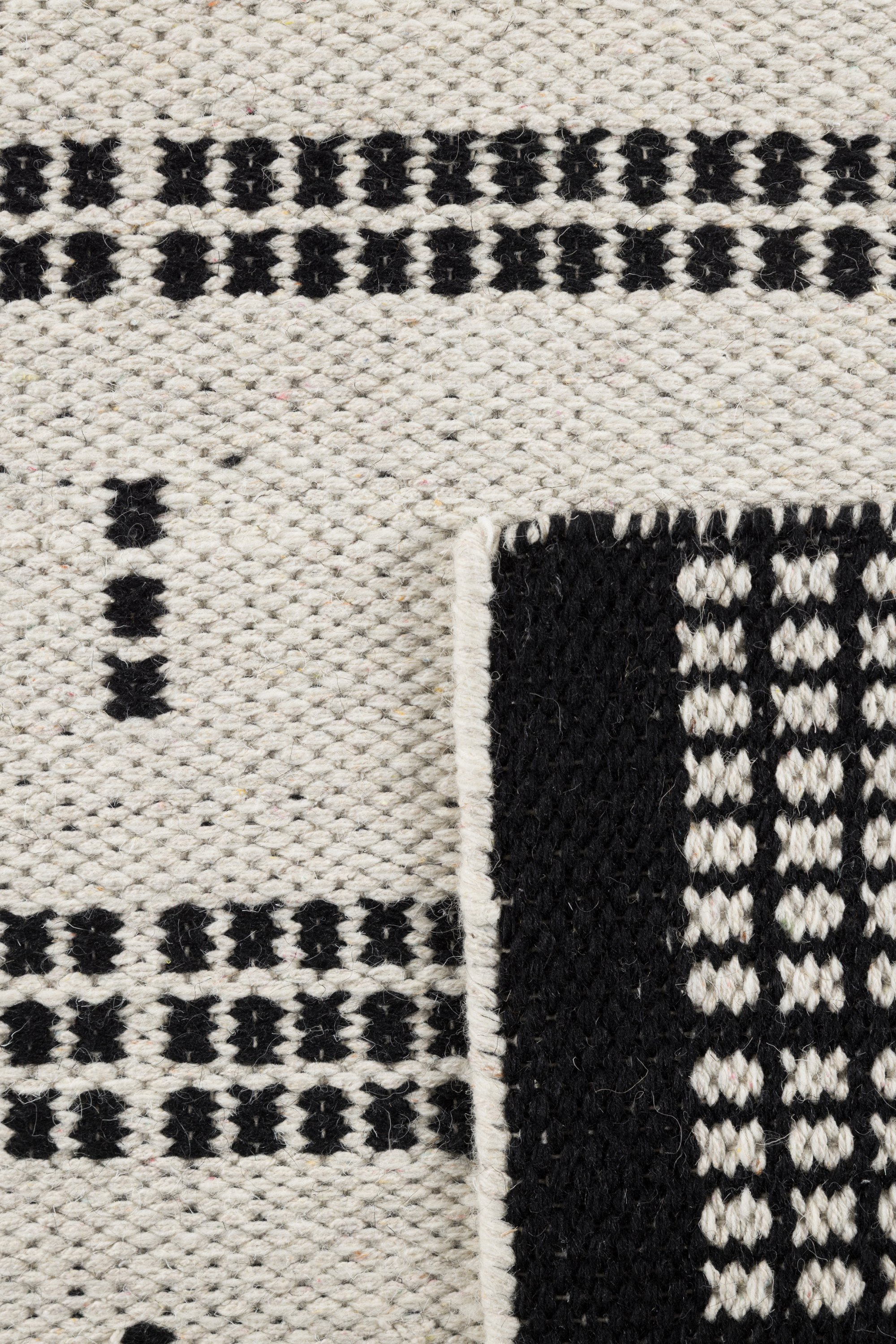 Close up of a White wool and cotton rug with a black geometric pattern inspired by the Manhattan skyline at night