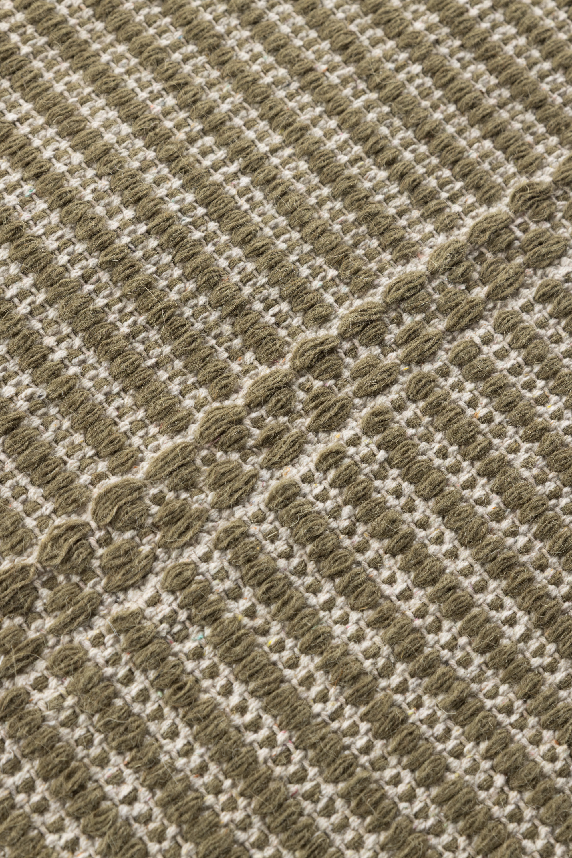 a close up of the pile of a wool and cotton runner rug in dark green moss tones featuring a design inspired by ancient irish script