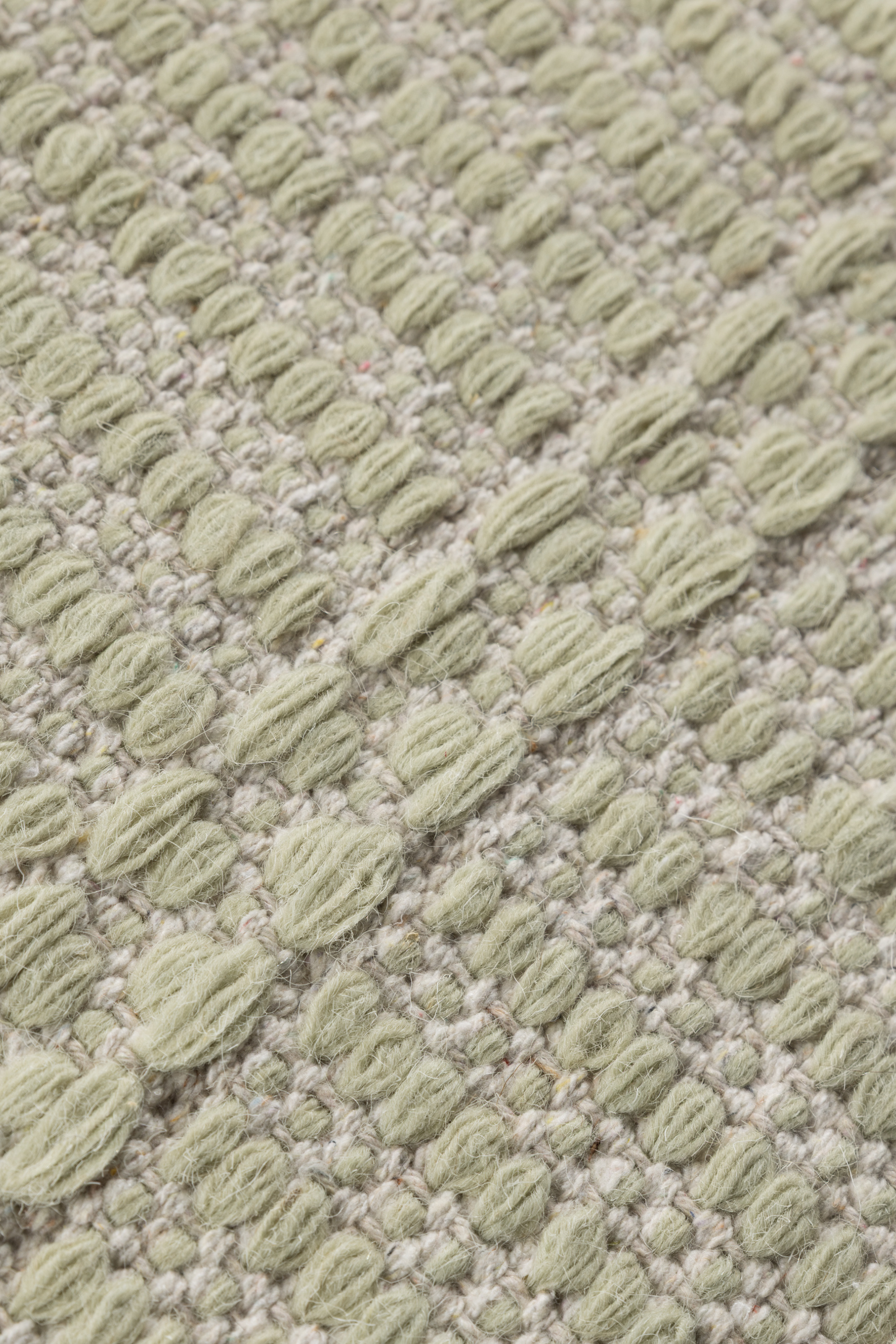 a close up of a wool and cotton runner rug in soft olive hues featuring a design inspired by ancient irish script