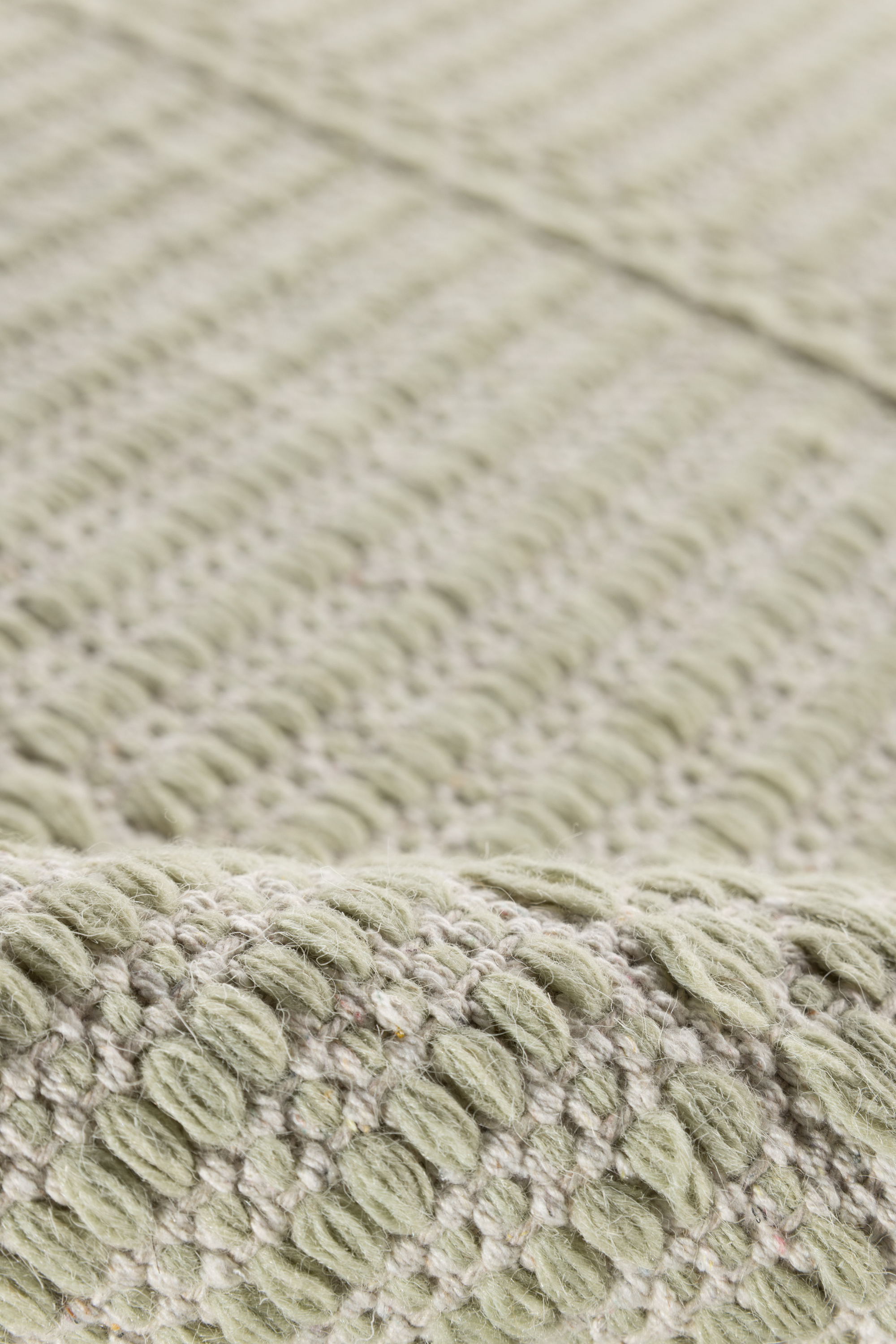 a close up of the pile on a wool and cotton runner rug in soft olive hues featuring a design inspired by ancient irish script