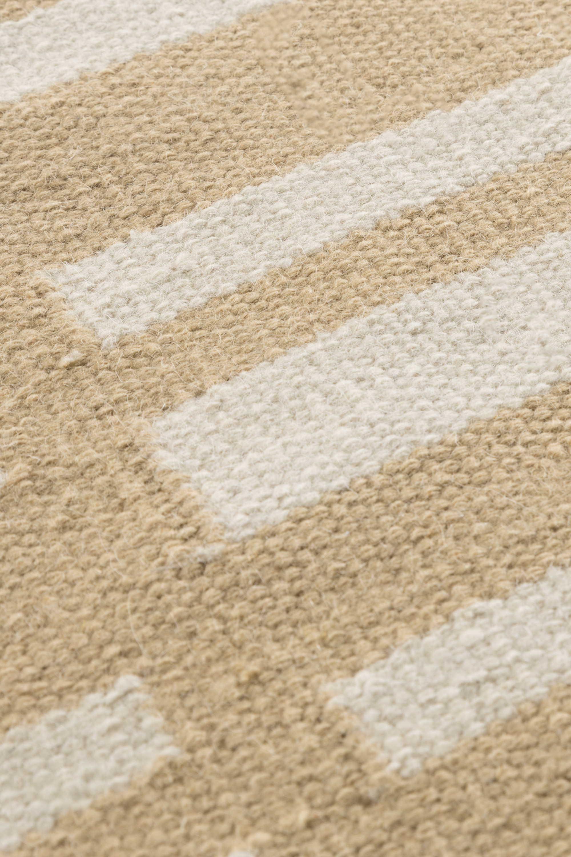 a closeup of the pile of a beige and straw toned wool and cotton rug featuring an irregular linear pattern