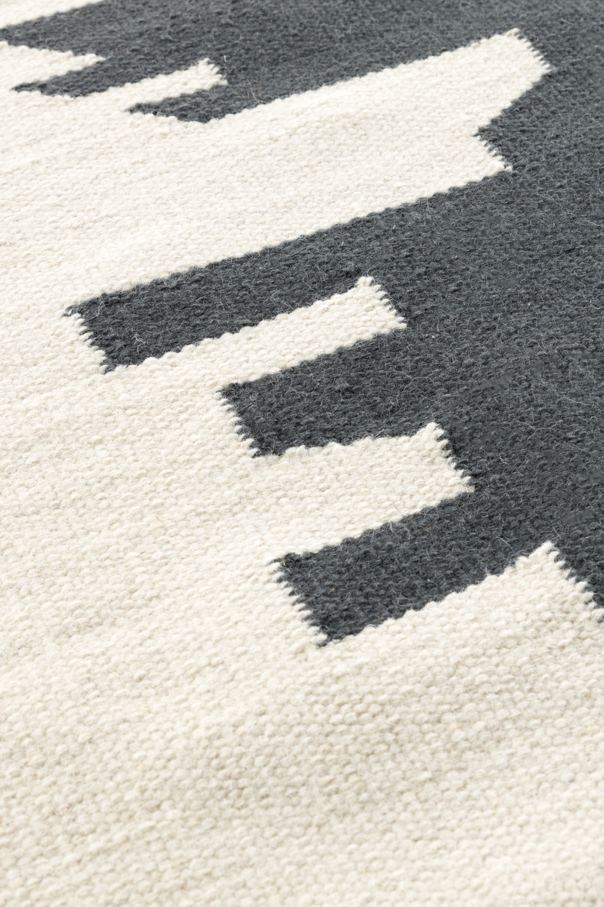 a closeup of a black and white wool and cotton rug featuring a monochromatic modern abstract design