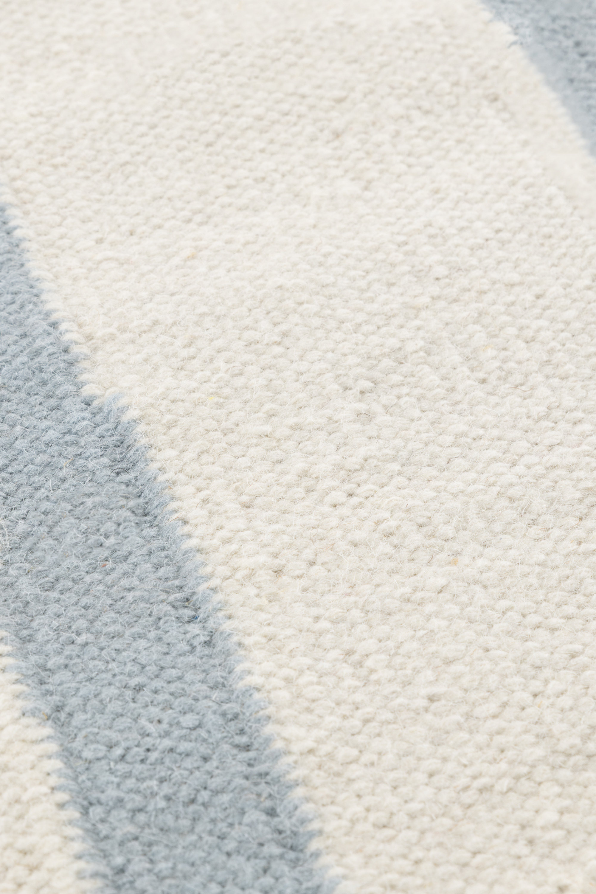 a closeup of the pile of a neutral ivory wool and cotton flatweave rug featuring blue ripple linear lines