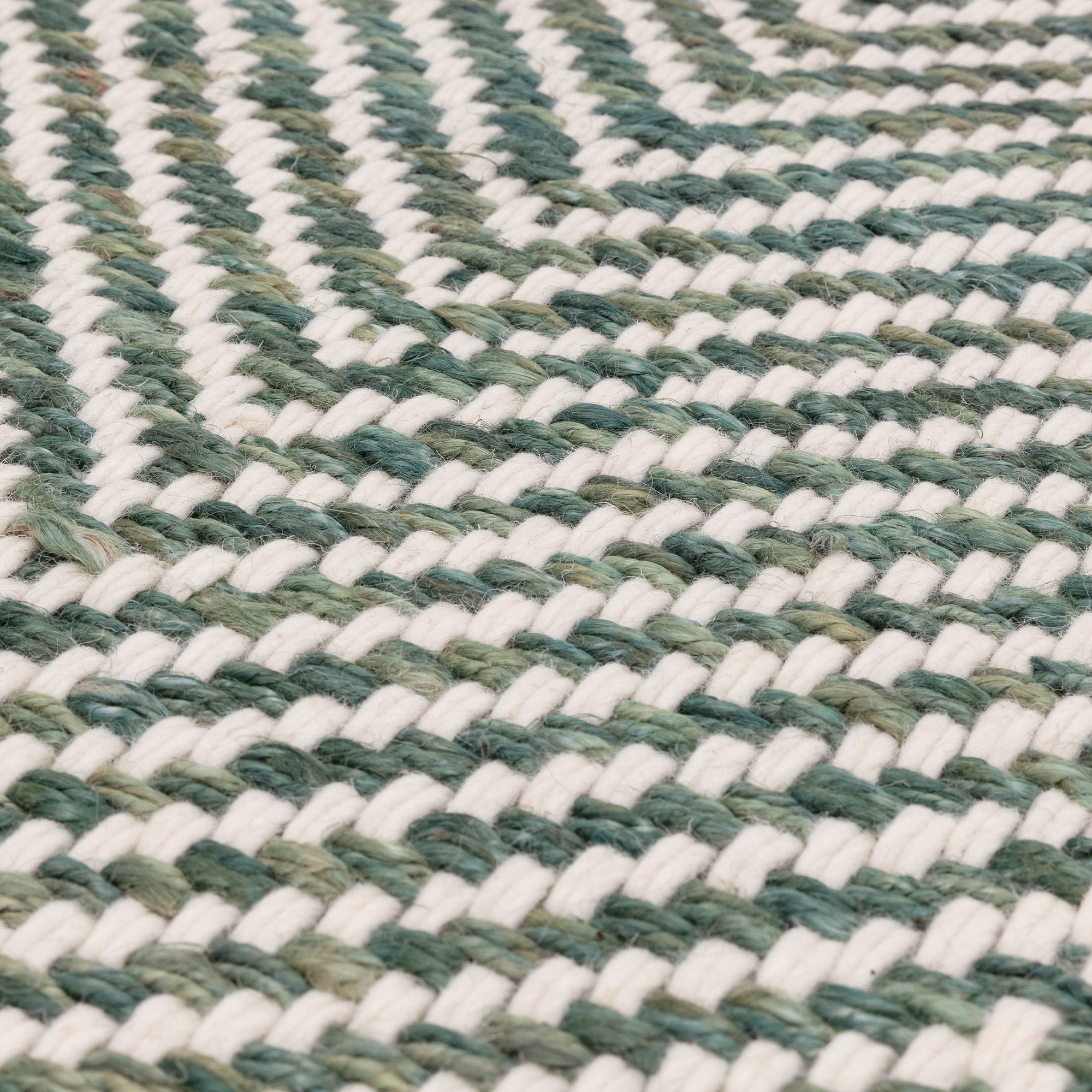 Textured woven rug with green and cream chevron pattern