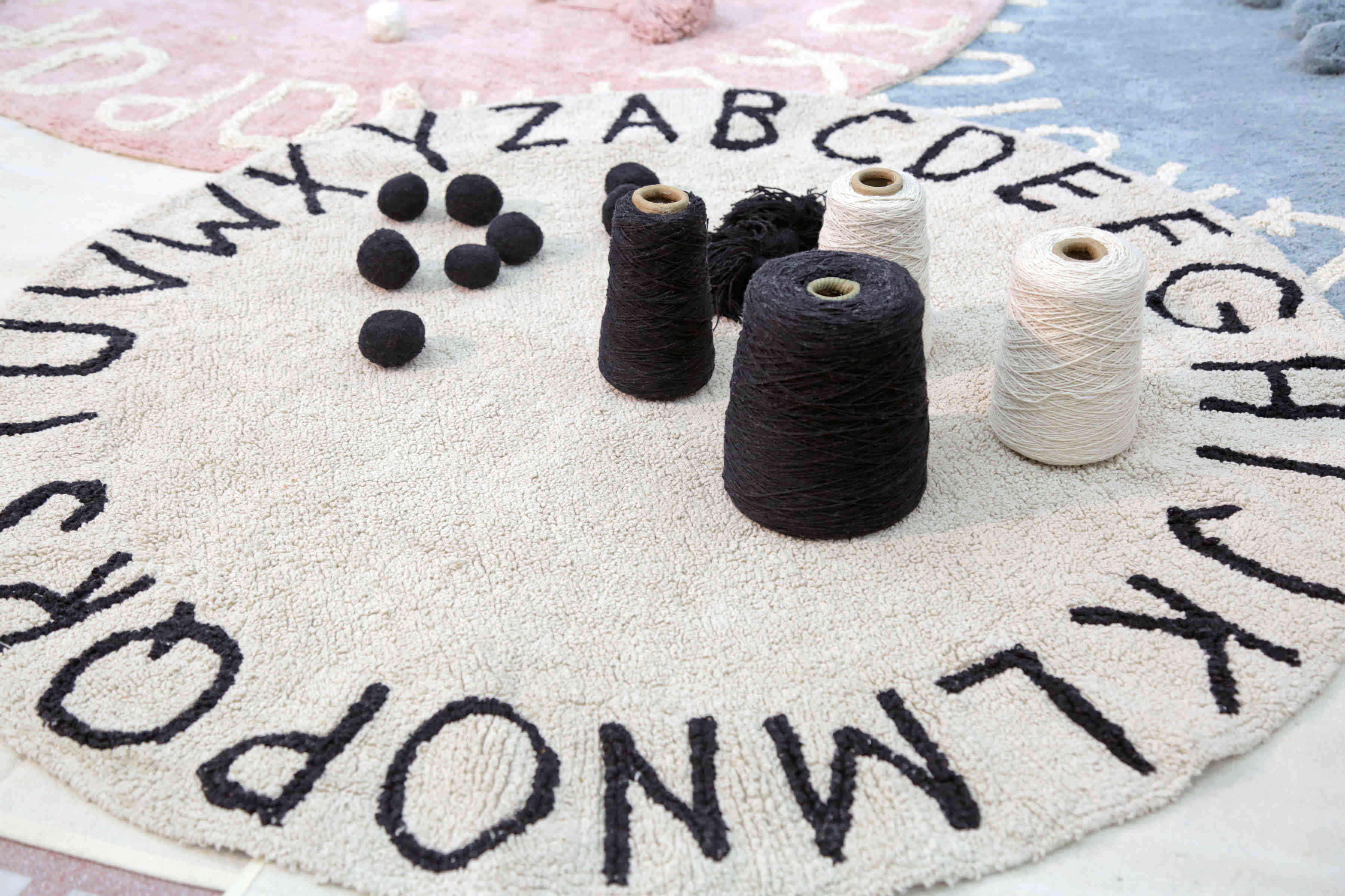 Circular white cotton rug decorated with a black alphabet border