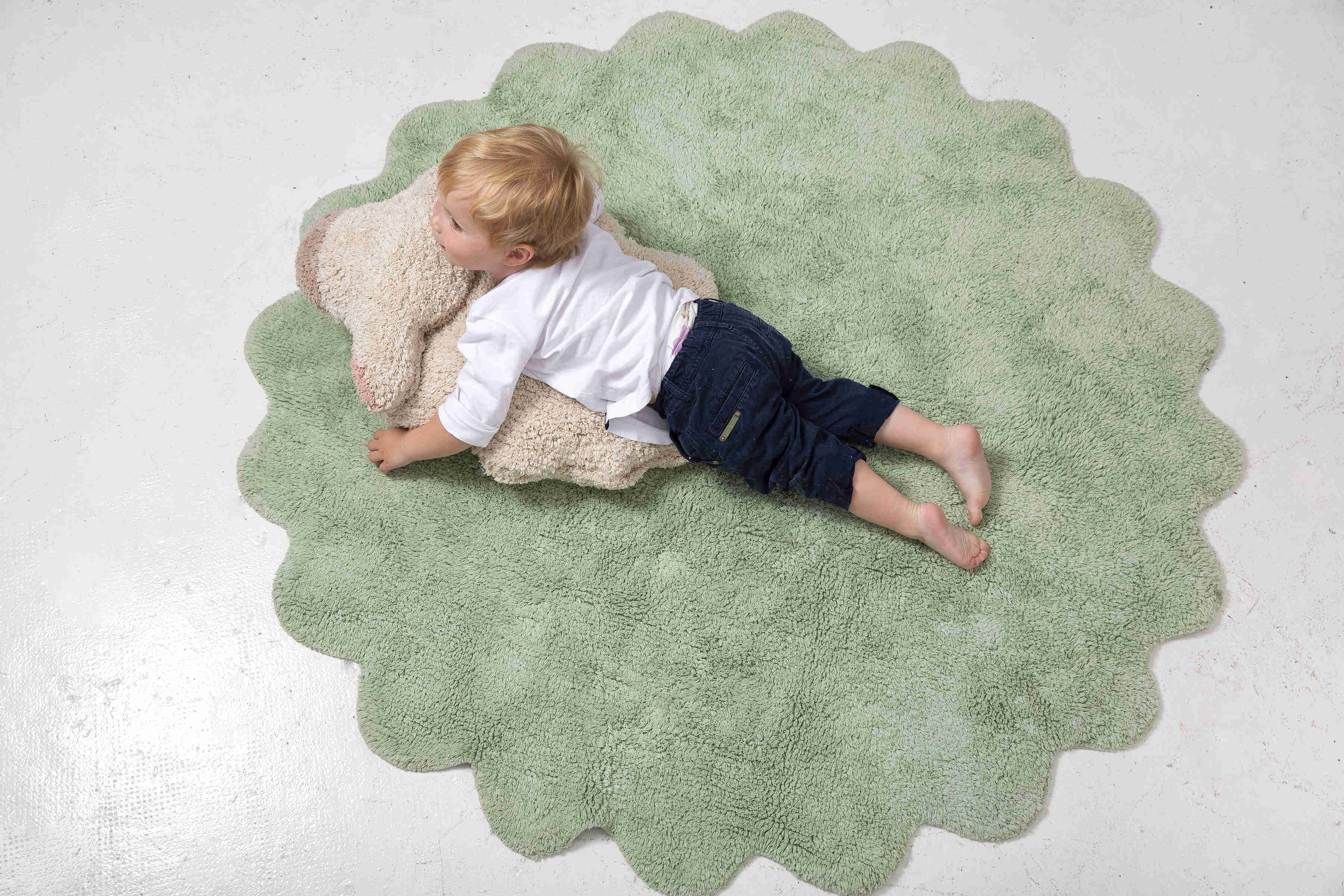 Circular green cotton rug with scalloped edge and detachable cream sheep cushion