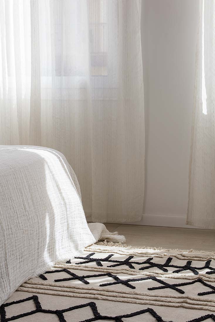 Rectangular beige cotton rug decorated with a black moroccan tribal design and a fringed border