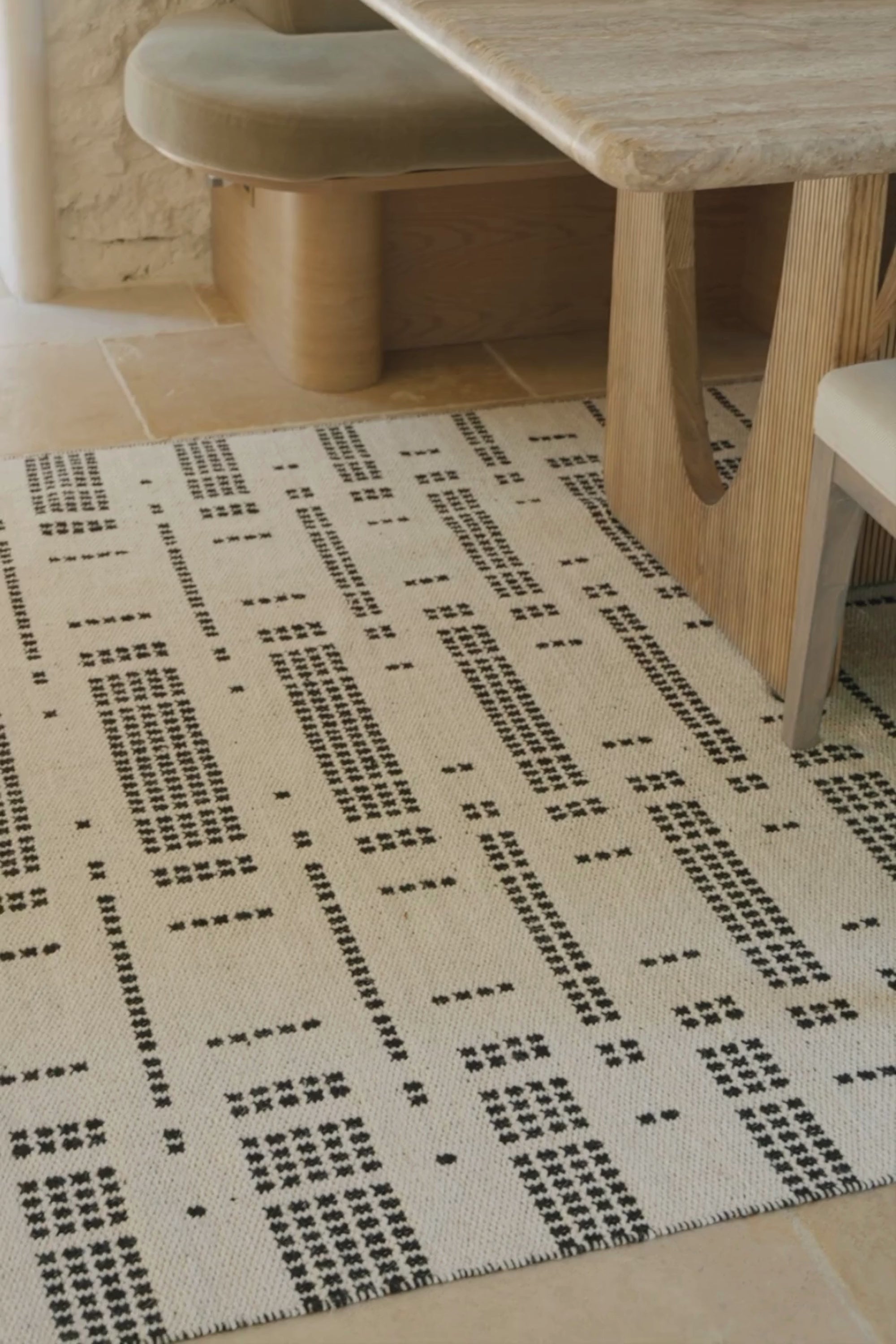 A video of a white wool and cotton rug with a black geometric pattern inspired by the Manhattan skyline at night placed under a dining table 